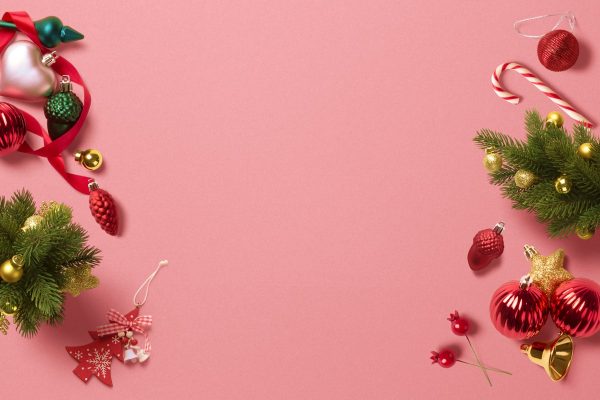 Christmas ornaments, a candy cane, pine sprigs and ribbon arranged around the edges of a pink background.