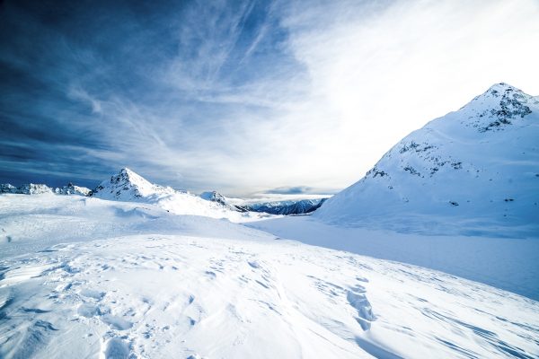 Snow-covered mountain peaks and a wide snowfield under a deep blue sky with wispy clouds.
