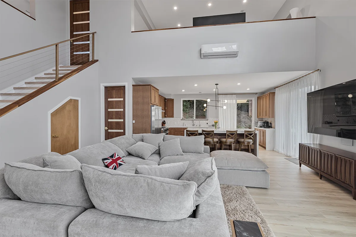 Airy living room with a gray sectional sofa, high ceilings and an open kitchen