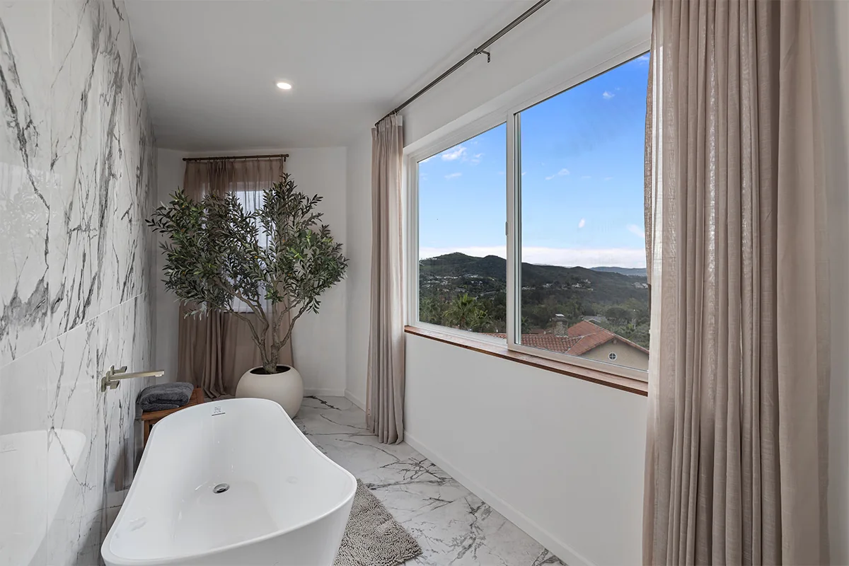 Freestanding bathtub beside a large window overlooking the green hills